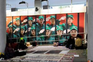 Sunday is a day off for many domestic helpers in Hong Kong, and Central becomes a place to gather. In this tunnel at the heart of the district, groups settled in as they always do, laying out mats, sharing food, and passing time together. Behind them, an enormous mural advertises a local theatre production, its staged expressions frozen in intensity. Undisturbed by the drama on display, life unfolded quietly in front of it, grounded in routine, conversation, and the simple act of being together.