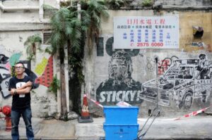 Behind the shopping arcades and restaurants in Causeway Bay, the back alleys hold a different layer of the city. Elaborate graffiti spreads across the walls, carrying its own narratives. I was framing the illustrated cop against the real police line when a man stepped into view and held his pose. He seemed to belong to neither side, yet completed the scene, standing between the drawn authority and the quiet tension of the street.